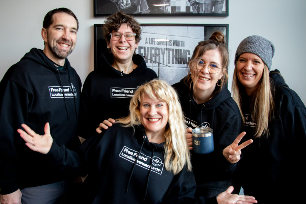 One man and four women are posing for a photo in matching hoodies